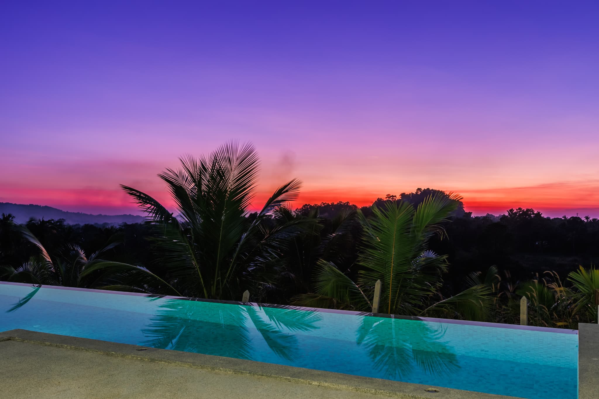 Poolkante mit Palmensilhouetten bei Sonnenuntergang